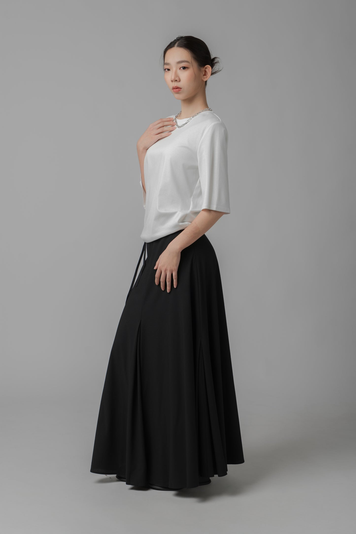 Woman wearing a white asymmetric top and black A-line skirt on a gray background