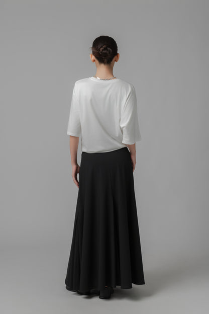 Woman wearing a white asymmetric top and black A-line skirt on a gray background