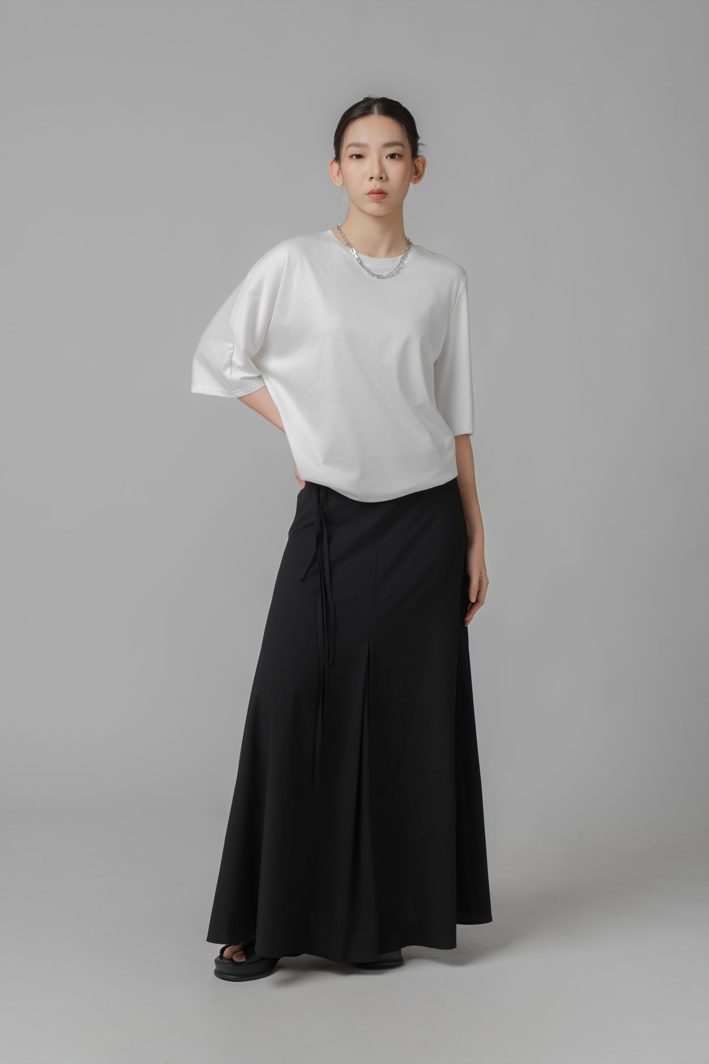 Woman wearing a white asymmetric top and black A-line skirt on a gray background