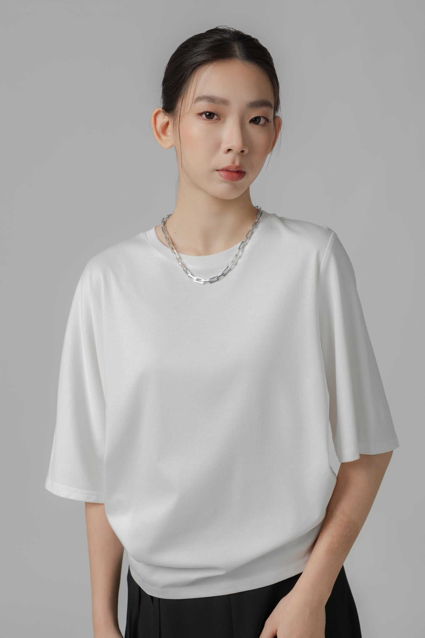 Woman wearing a white asymmetric top and black A-line skirt on a gray background