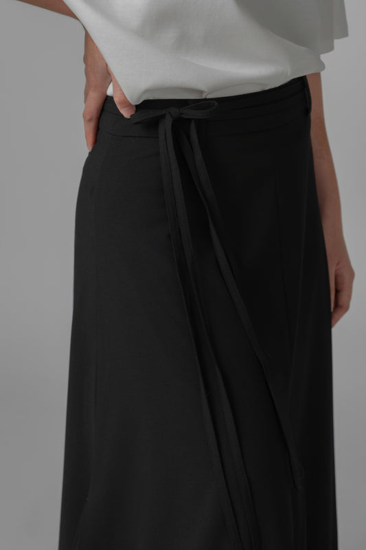 Person wearing black A-line skirt with waist ties on a gray background