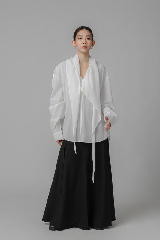 Person wearing a white oversize shirt with scarf collar and a black A-line skirt on a gray background
