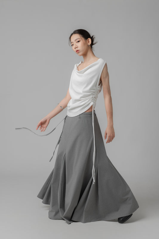Woman wearing a white sleeveless top and a long gray A-line voluminous skirt on a plain background