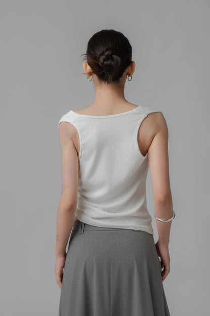 Woman showing the back of a white sleeveless wide-neck top with adjustable side string, paired with a grey skirt