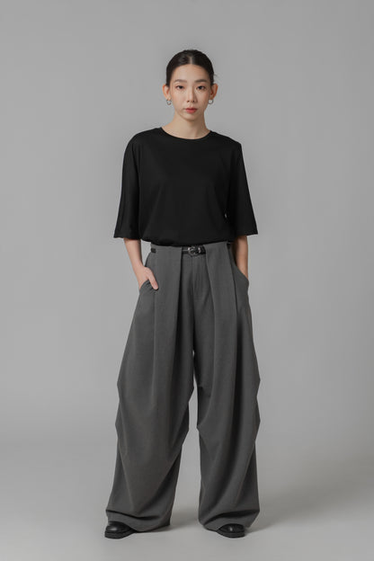 Person wearing a black asymmetric T shirt and gray wide-leg pants with a leather belt