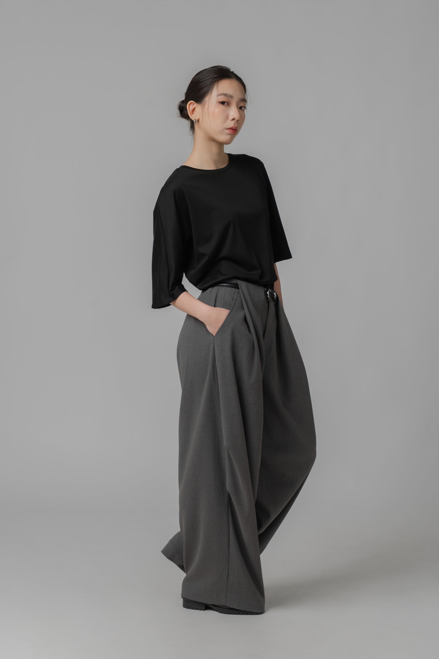 Person wearing a black asymmetric T shirt and gray wide-leg pants with a leather belt