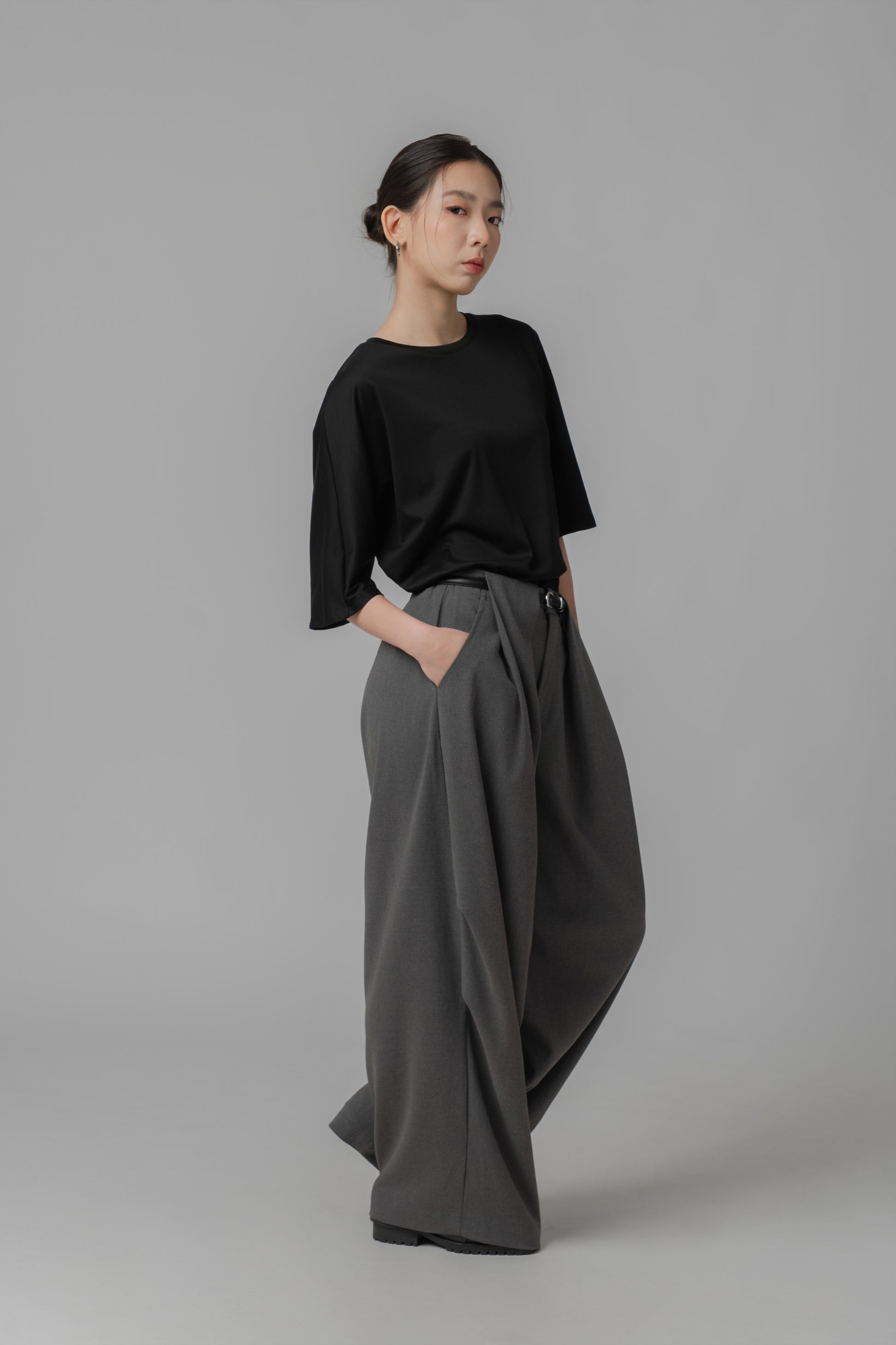 Person wearing a black asymmetric T shirt and gray wide-leg pants with a leather belt
