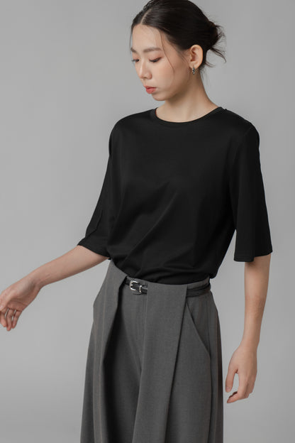 Woman wearing a black asymmetric T shirt and gray wide-leg pants with a leather belt