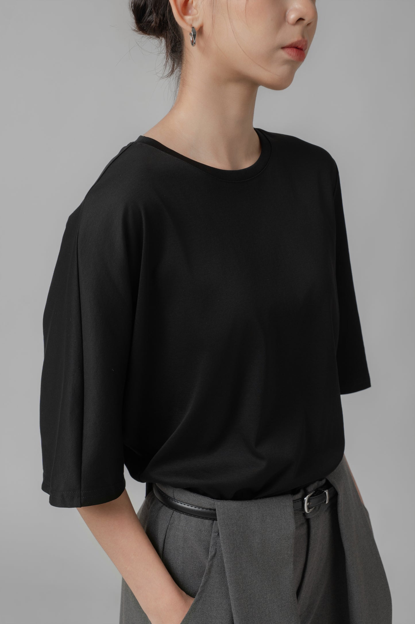 Person wearing a black asymmetric T shirt and gray wide-leg pants with a leather belt