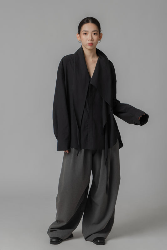 Person wearing a black oversize shirt with scarf collar and gray pants on a gray background