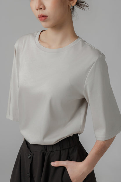 Person wearing a light gray asymmetric T shirt and black wide-leg pants on a plain background