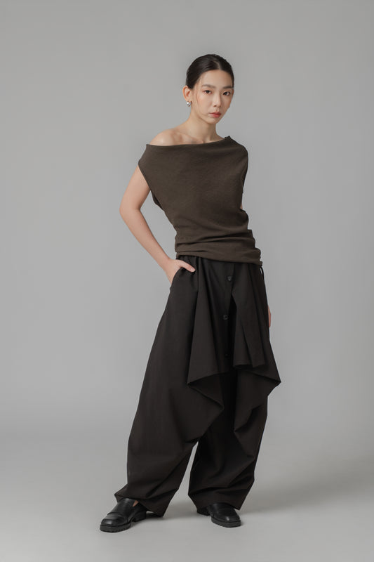 Woman wearing a brown off-shoulder top and black wide-leg pants layered with front panels on a gray background