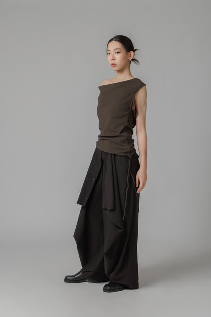 Woman wearing a dark brown sleeveless one-shoulder draped top with adjustable side string, paired with black wide leg trousers