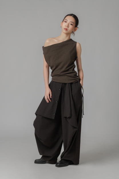 Woman wearing a dark brown sleeveless one-shoulder draped top with adjustable side string, paired with black wide leg trousers