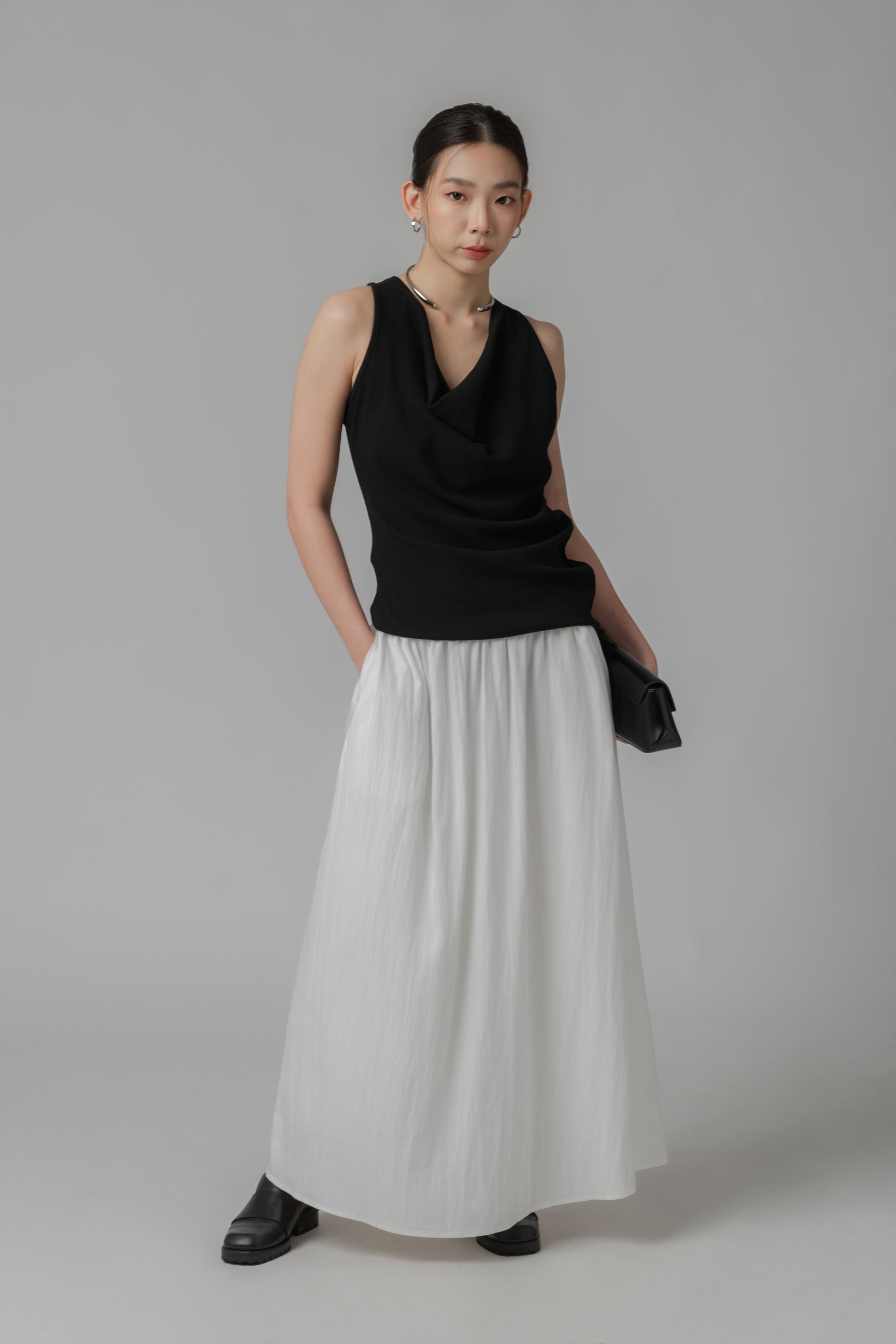 Woman wearing a black V-neck sleeveless top with adjustable side string, paired with a white skirt