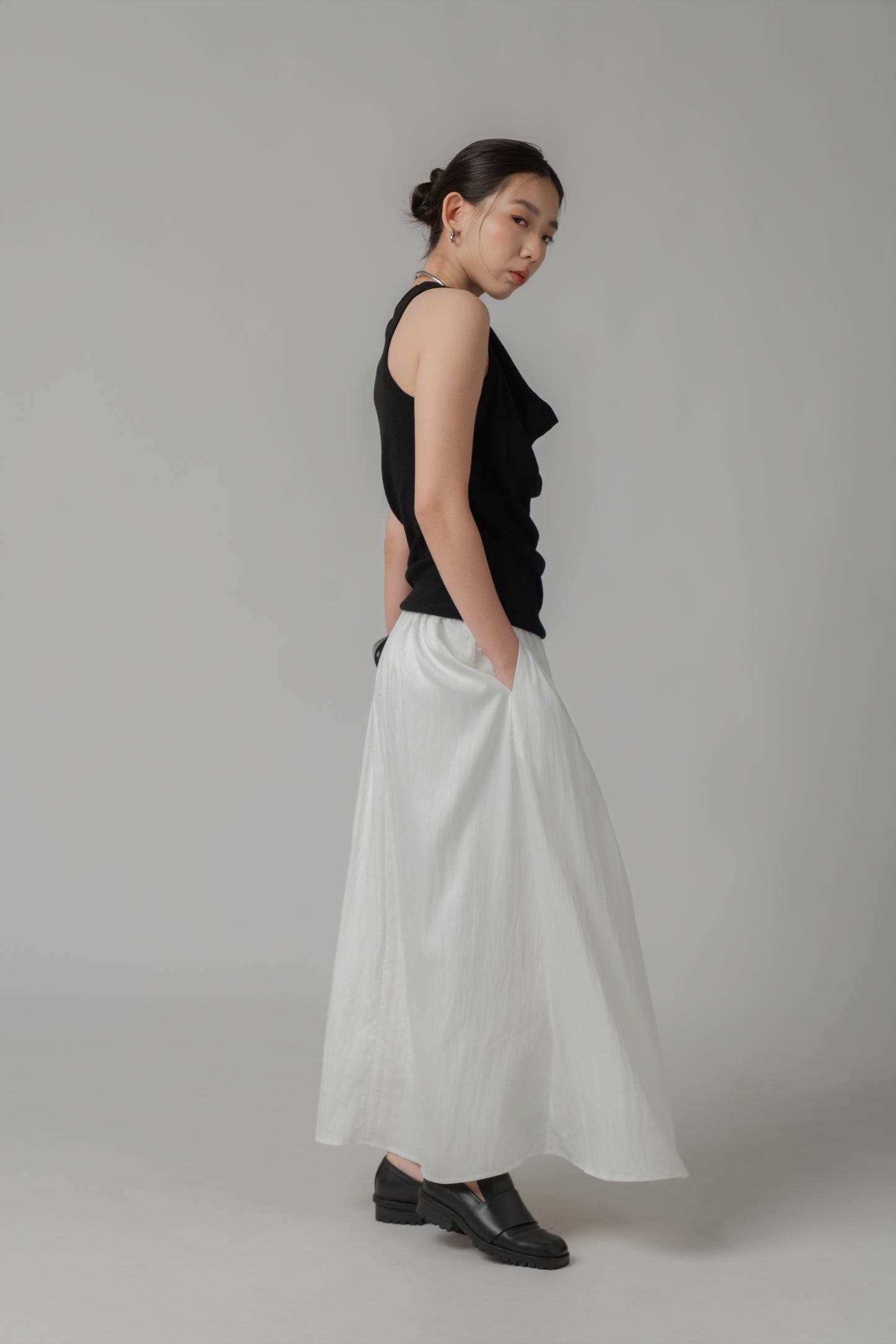 Woman wearing a black V-neck sleeveless top with adjustable side string, paired with a white skirt