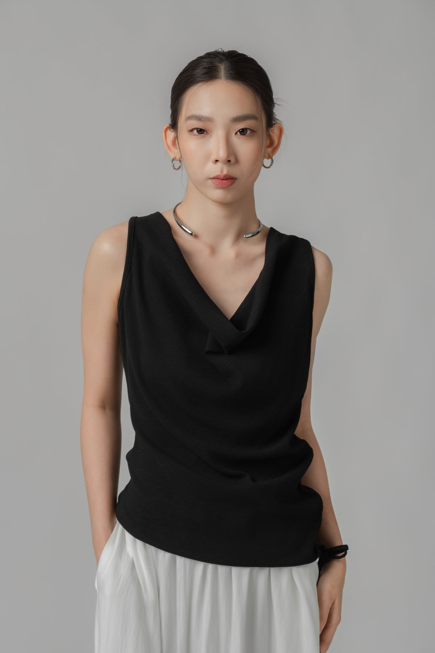 Woman wearing a black V-neck sleeveless top with adjustable side string, paired with a white skirt