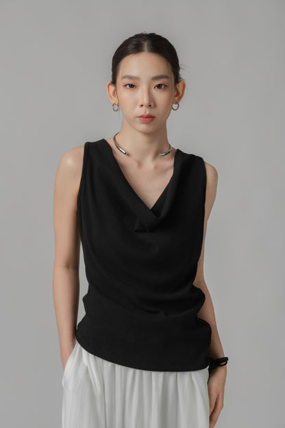 Woman wearing a black V-neck sleeveless top with adjustable side string, paired with a white skirt