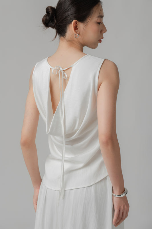 Woman wearing a sleeveless white V-neck top with a draped back