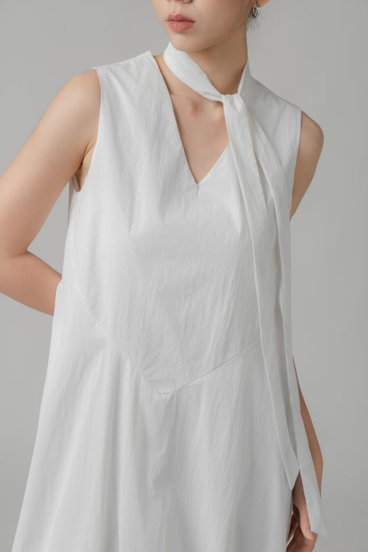 Woman wearing a white sleeveless bubble hem dress with scarf detail against a gray background
