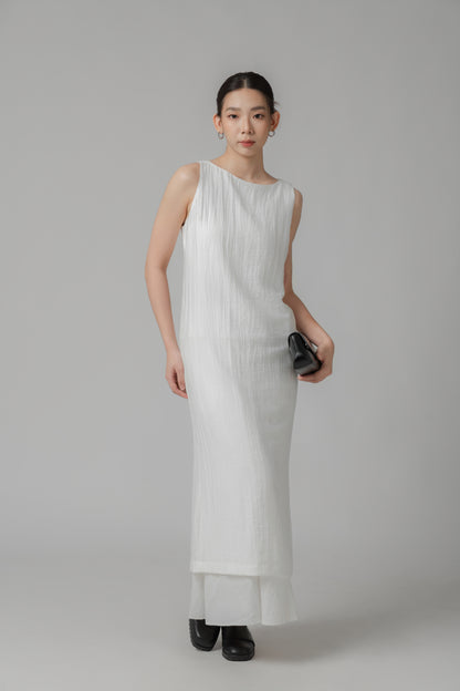 Woman wearing a white sleeveless crinkled column dress layered over a skirt and styled with a black leather bag