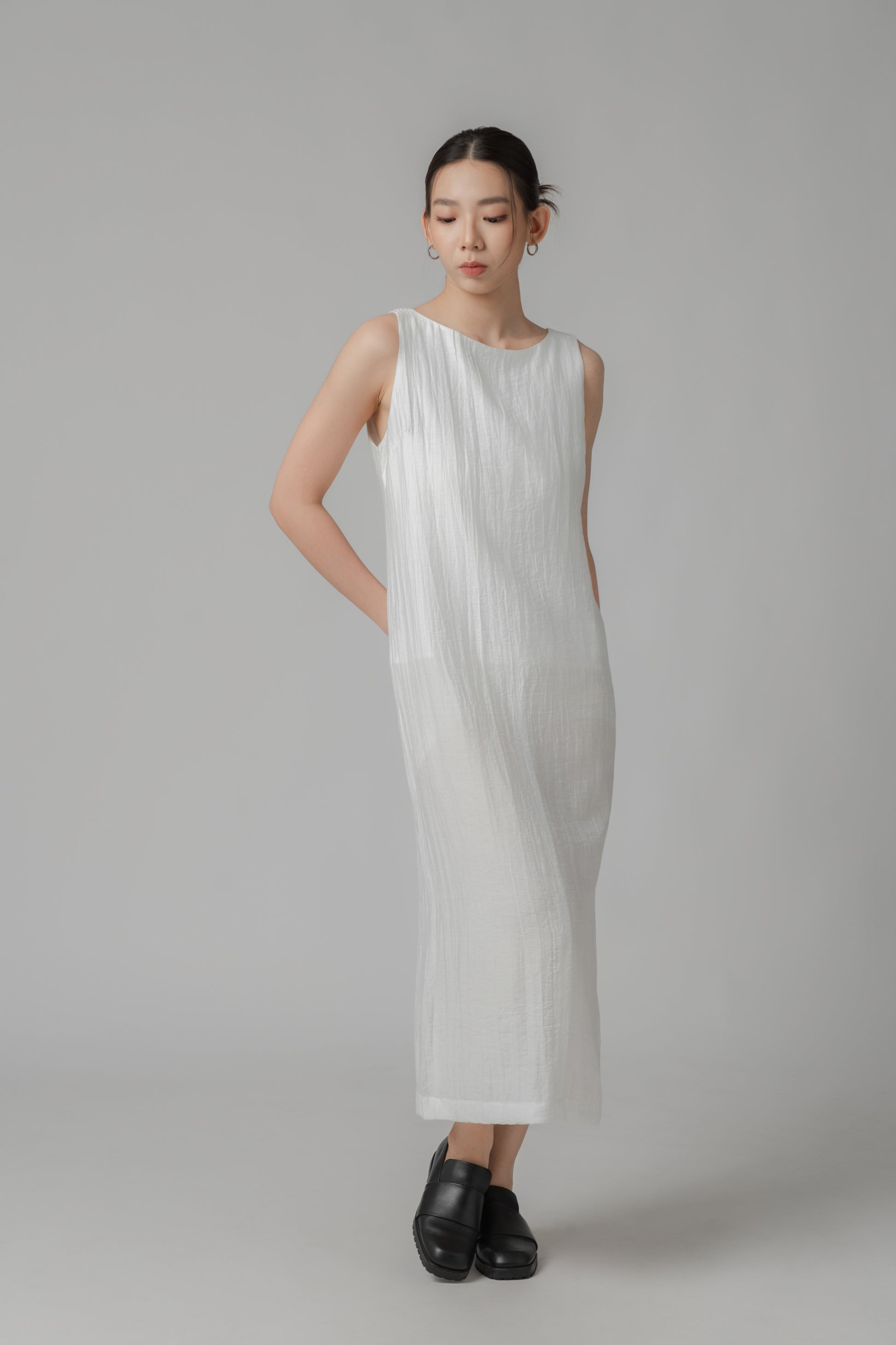 Woman showing the back of a white sleeveless crinkled column dress 