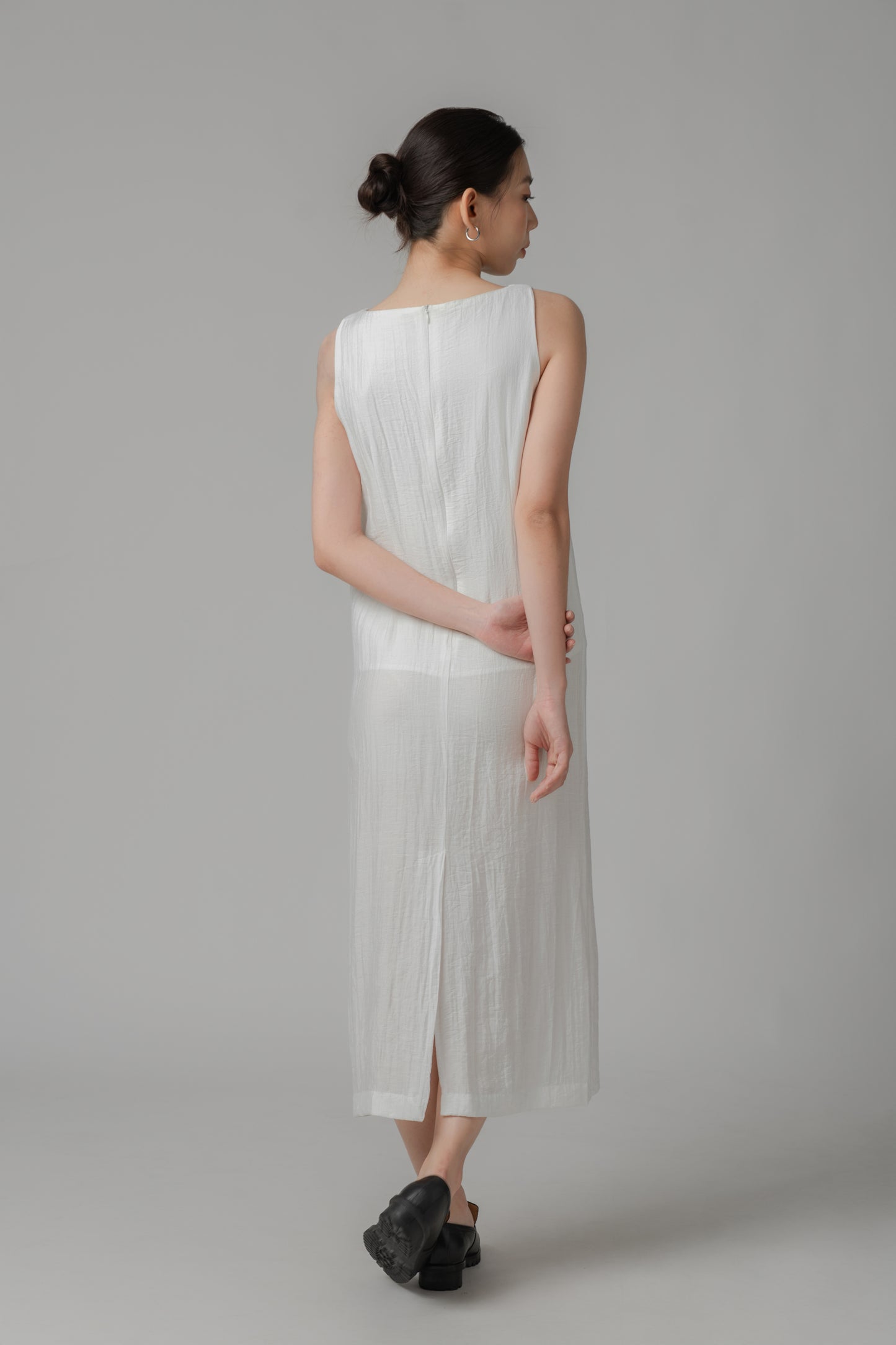 Woman showing the back of a white sleeveless crinkled column dress 