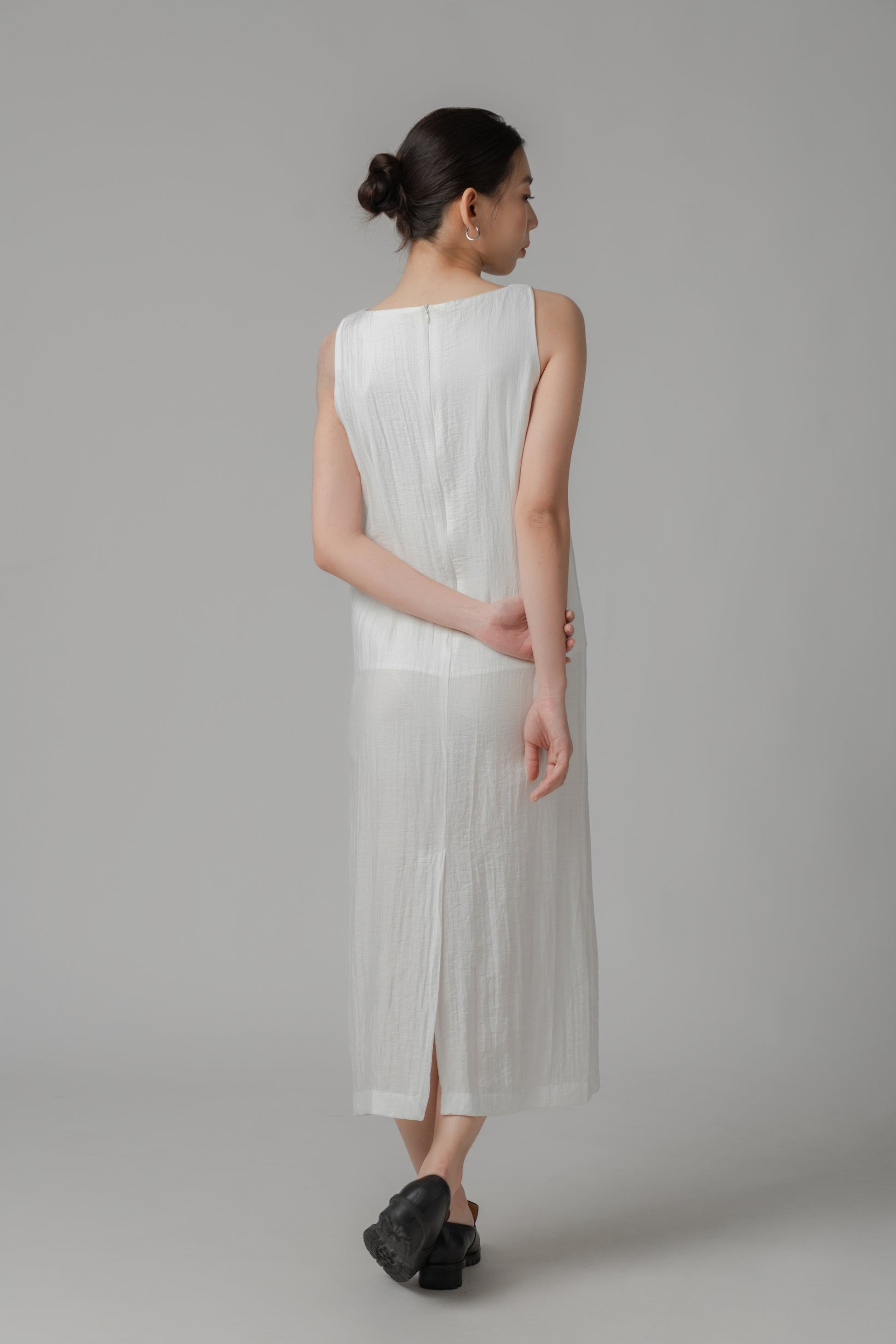 Woman showing the back of a white sleeveless crinkled column dress 