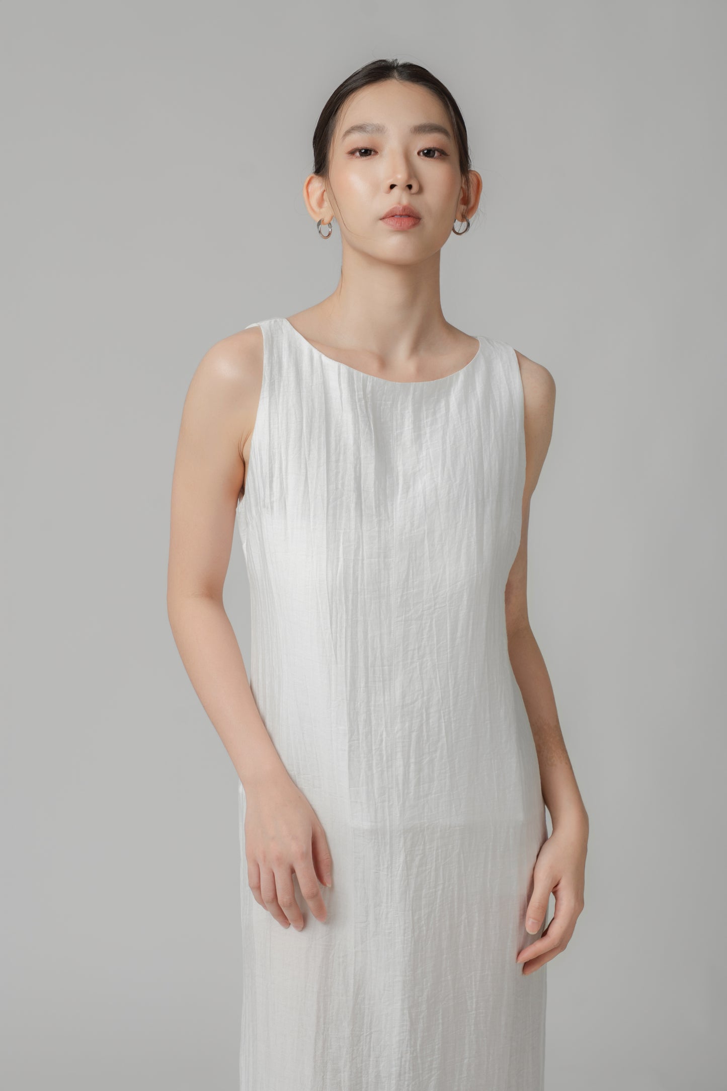 Woman wearing a white sleeveless crinkled column dress with boat neck