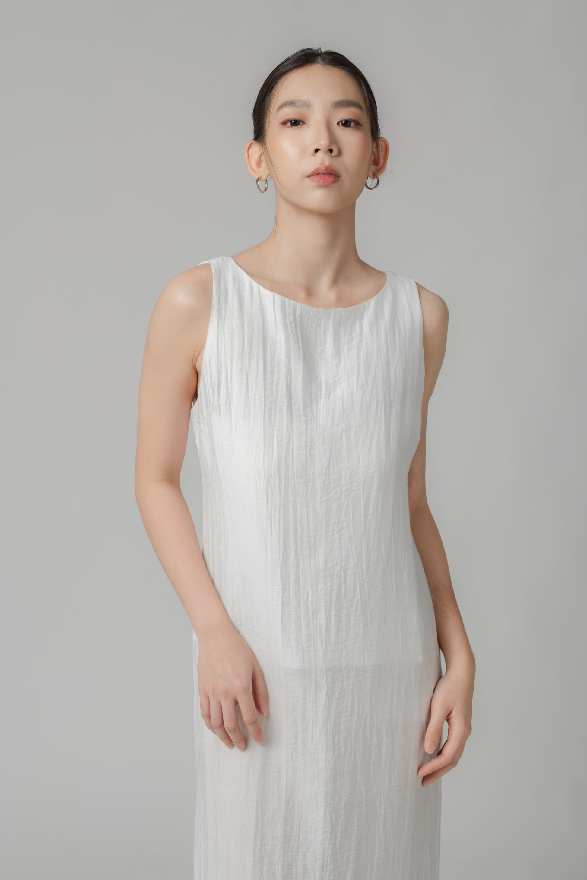 Woman wearing a white sleeveless crinkled column dress with boat neck